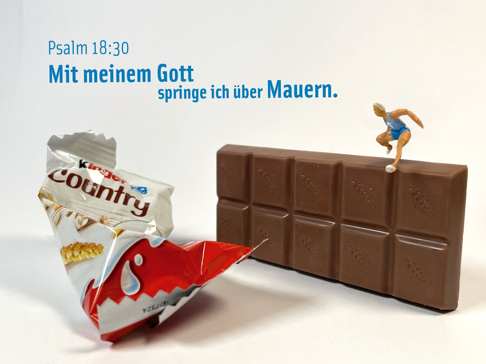 Eine Miniatur-Läuferin springt über eine Tafel Schokolade, daneben eine Riegelverpackung, dazu Psalm 18,30: „Mit meinem Gott springe ich über Mauern.“