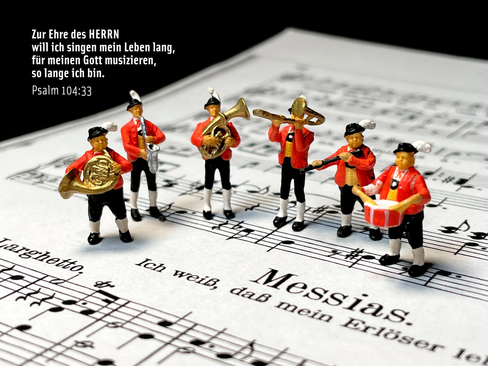 Eine Miniatur-Blaskapelle in roten Jacken musiziert auf den Noten des „Messias“, dazu Psalm 104,33: „Zur Ehre des HERRN will ich singen mein Leben lang“