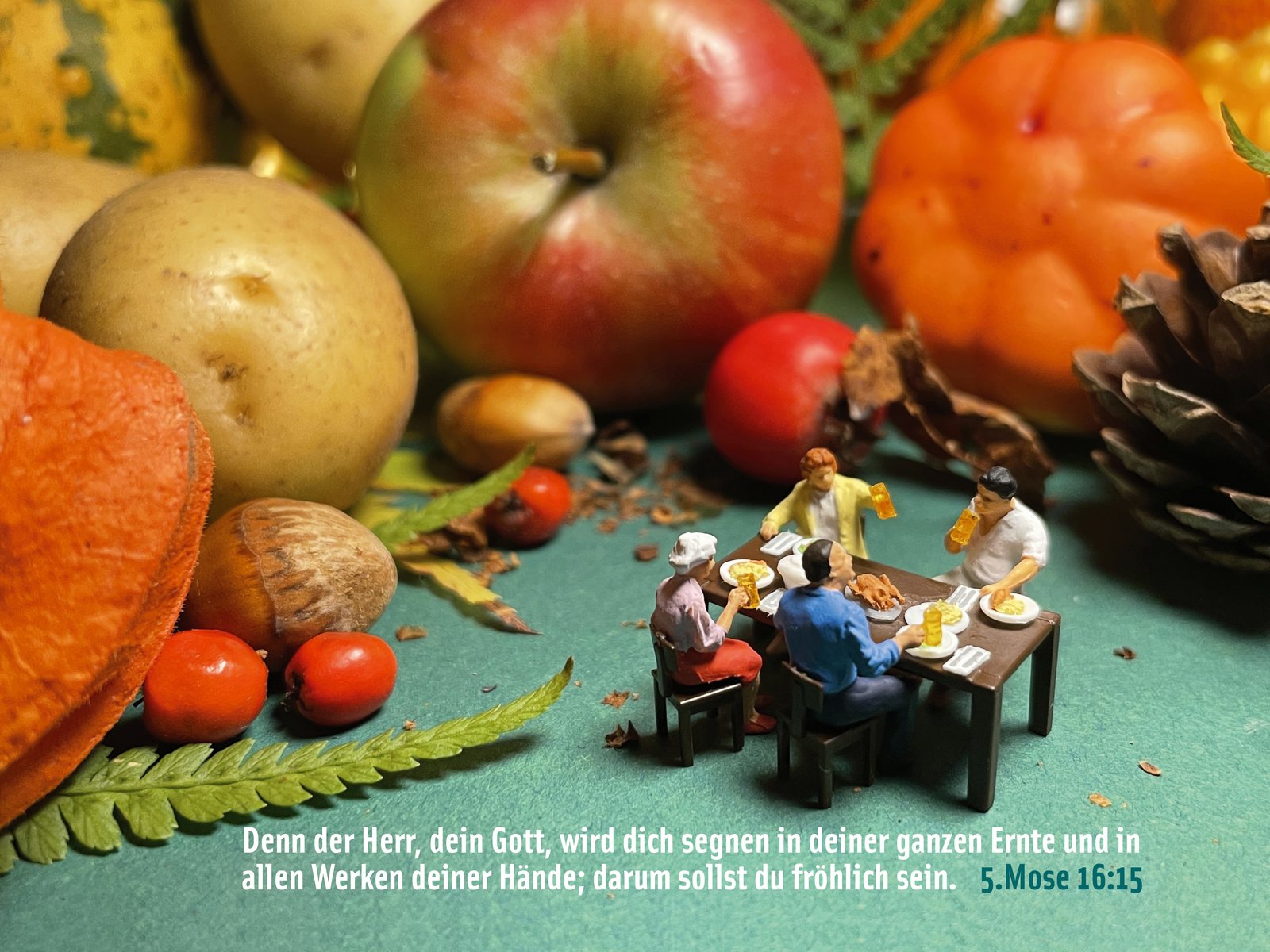 Eine Miniatur-Familie sitzt beim Essen an einem Tisch zwischen Äpfeln, Kürbissen und Kartoffeln, dazu 5. Mose 16,15 zum Erntedank