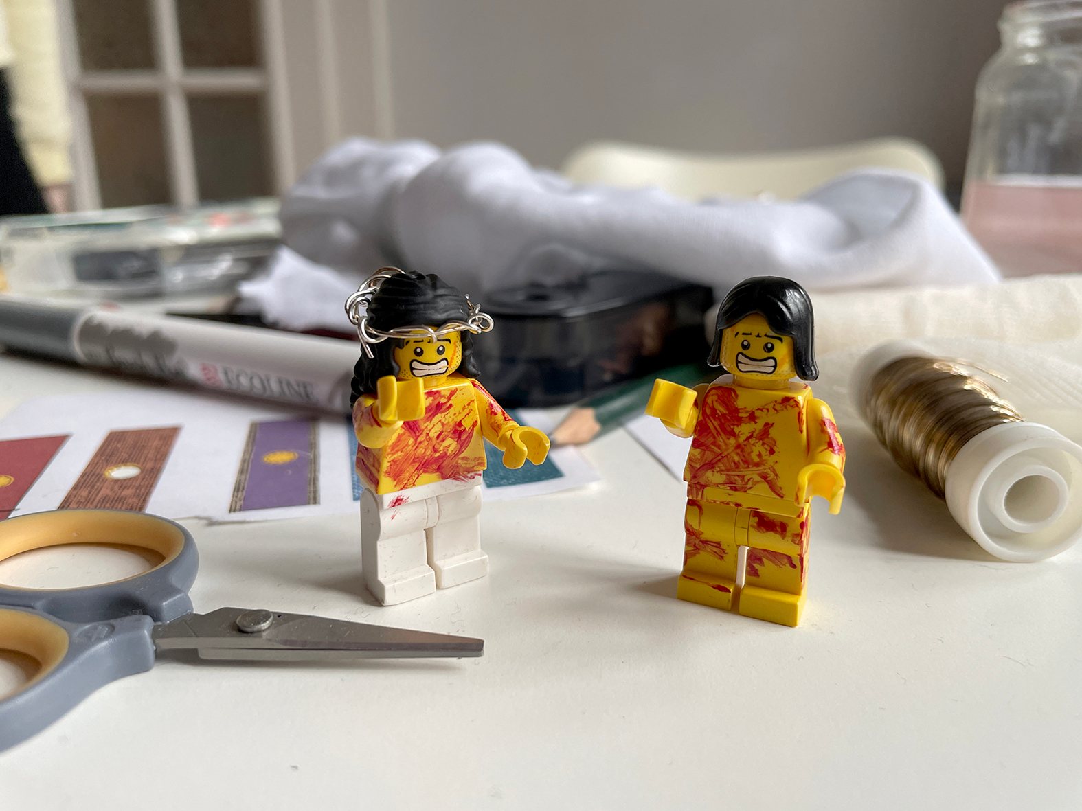 Zwei Jesus-Figuren für die Passionsgeschichte auf dem Arbeitstisch, eine mit Dornenkrone aus Draht, daneben Schere, Draht und Papierstreifen