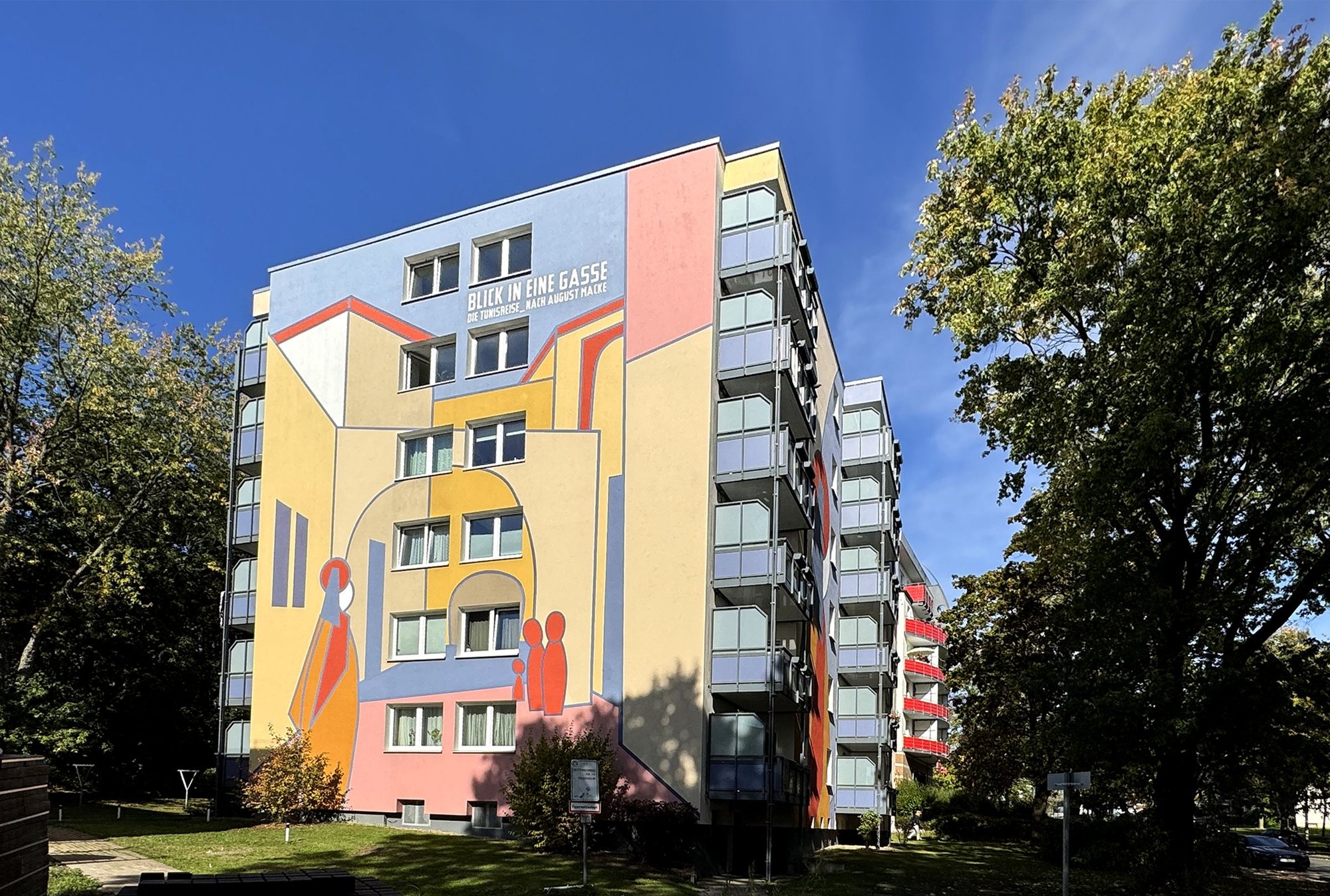 Hohes Wohnhaus im Rabenhof mit einer farbigen Fassadengestaltung in Gelb, Blau, Rosa und Rot unter blauem Himmel