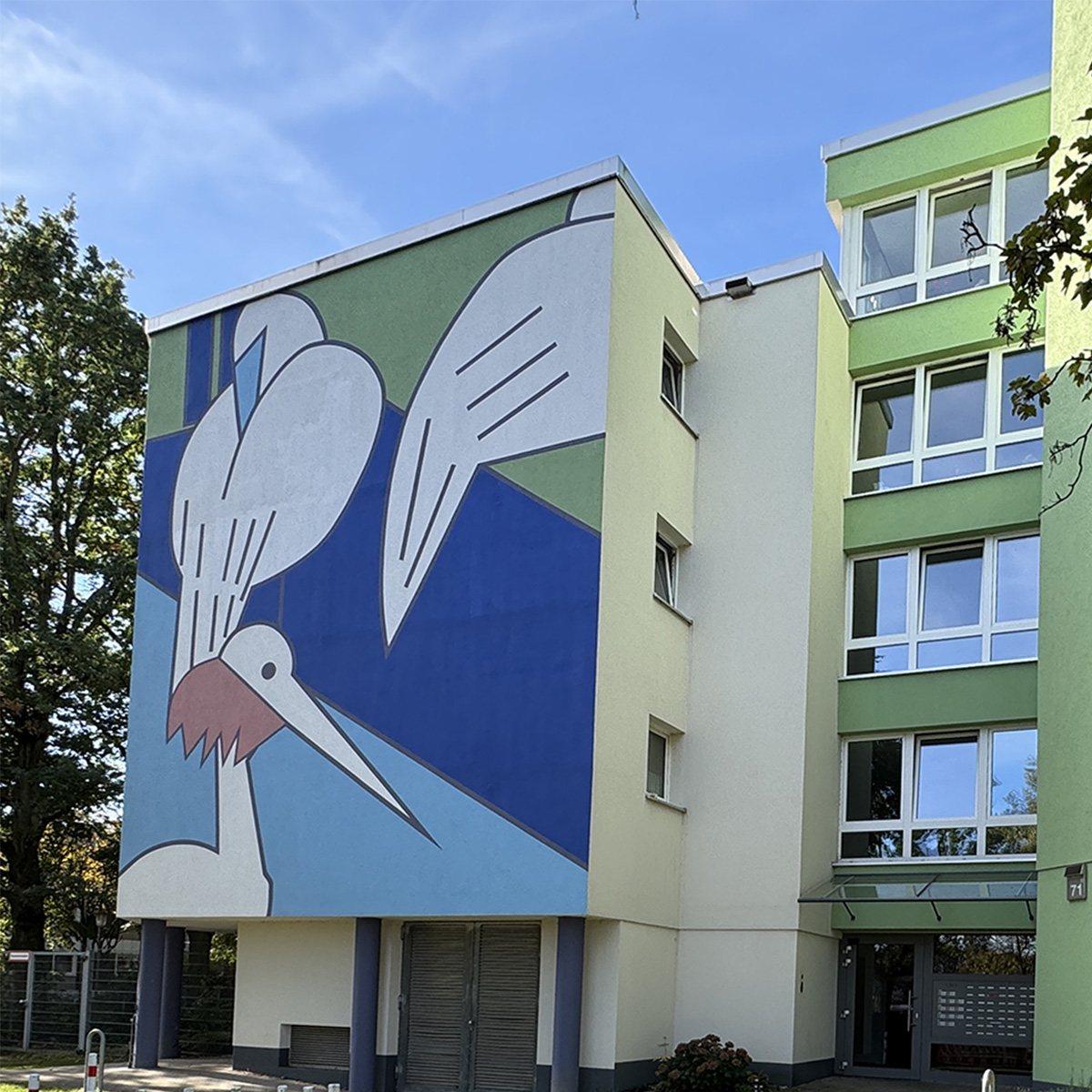 Fassadenbild im Rabenhof: ein großer weißer Vogel mit rotem Schnabel auf blauem und grünem Grund an der Giebelwand