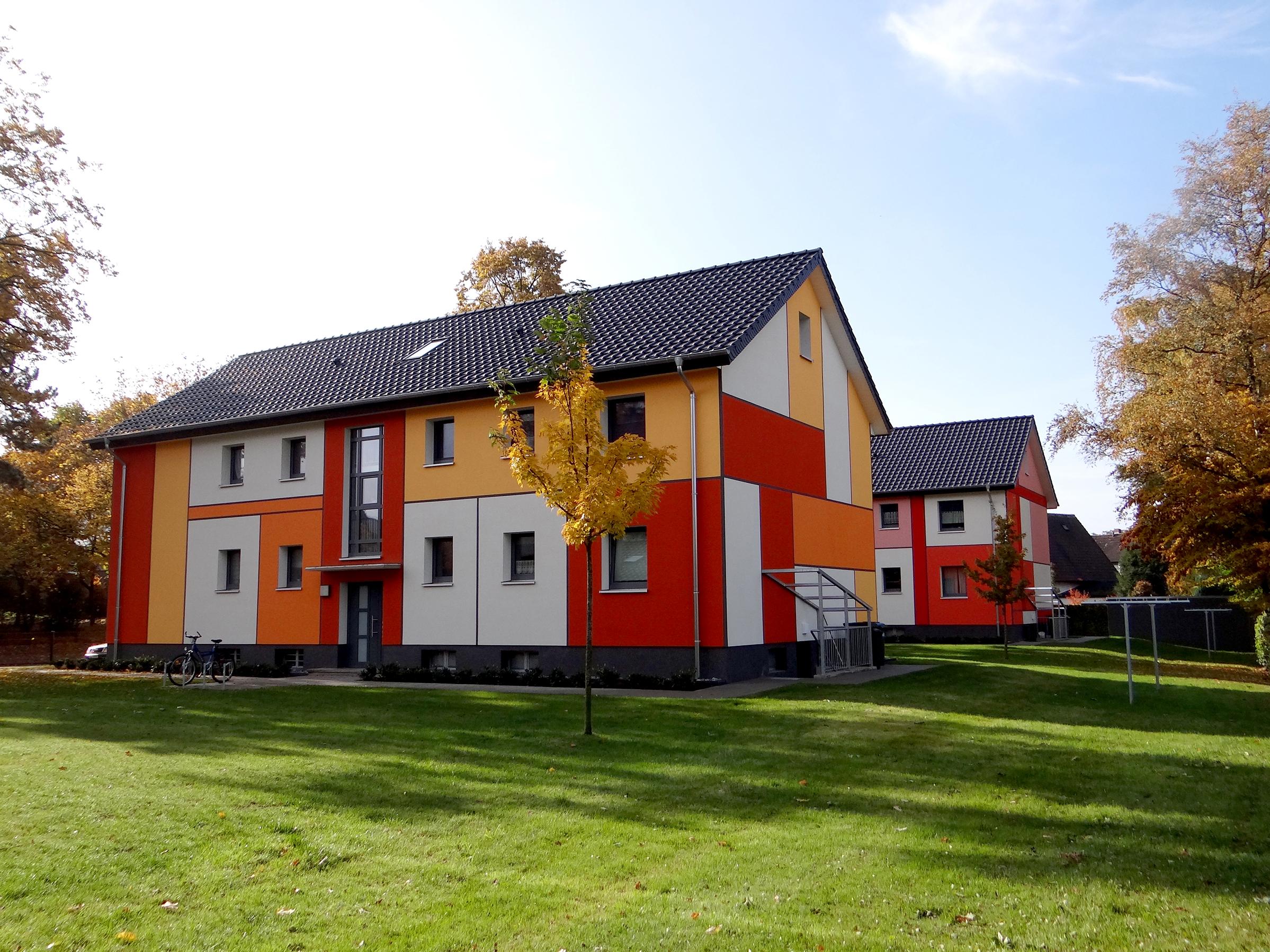 Mehrfamilienhäuser mit großen Farbflächen in Rot, Orange, Gelb und Grau auf einer Wiese im Herbst