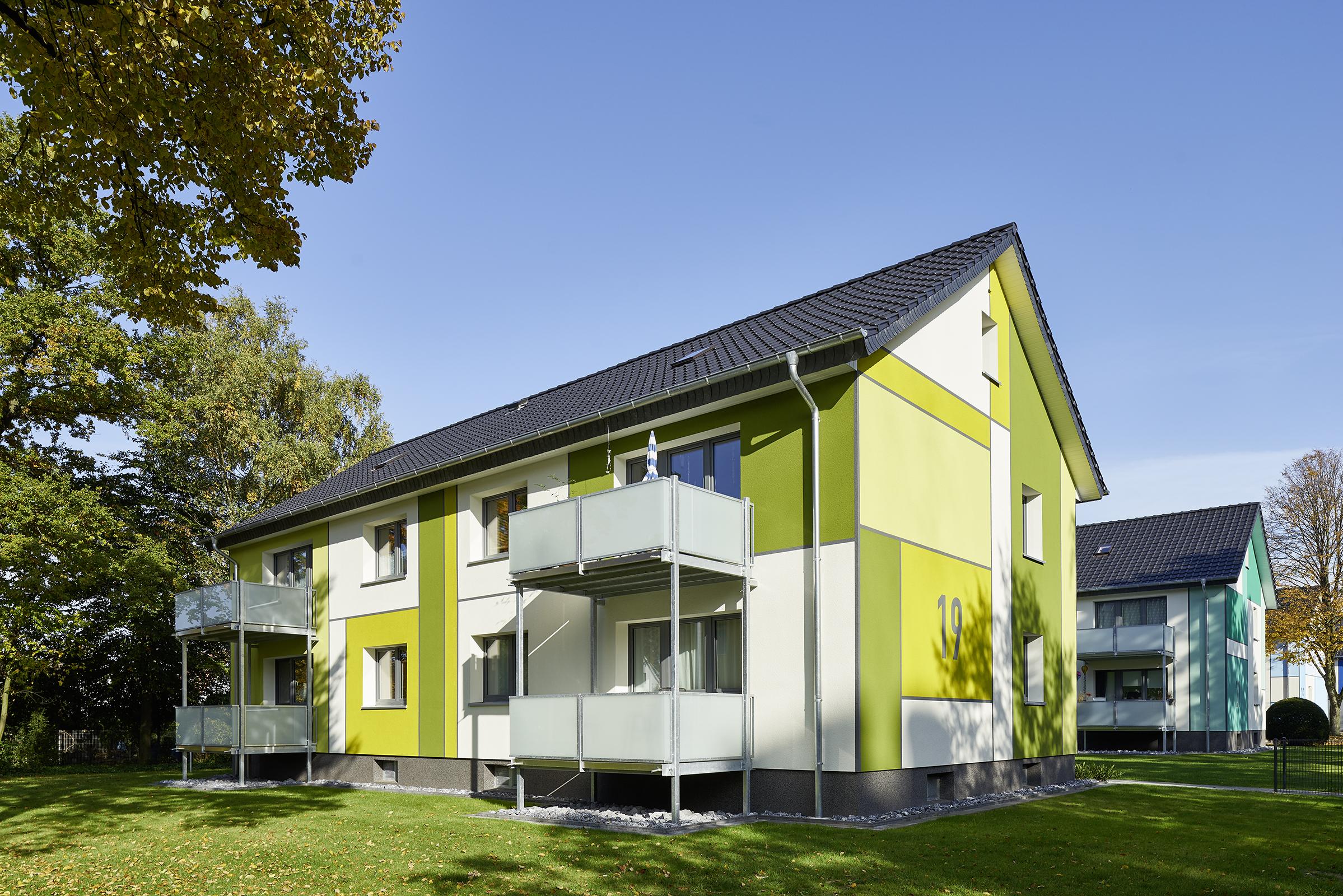 Mehrfamilienhaus mit Farbflächen in Hellgrün und Gelbgrün, im Hintergrund ein Haus in Türkis