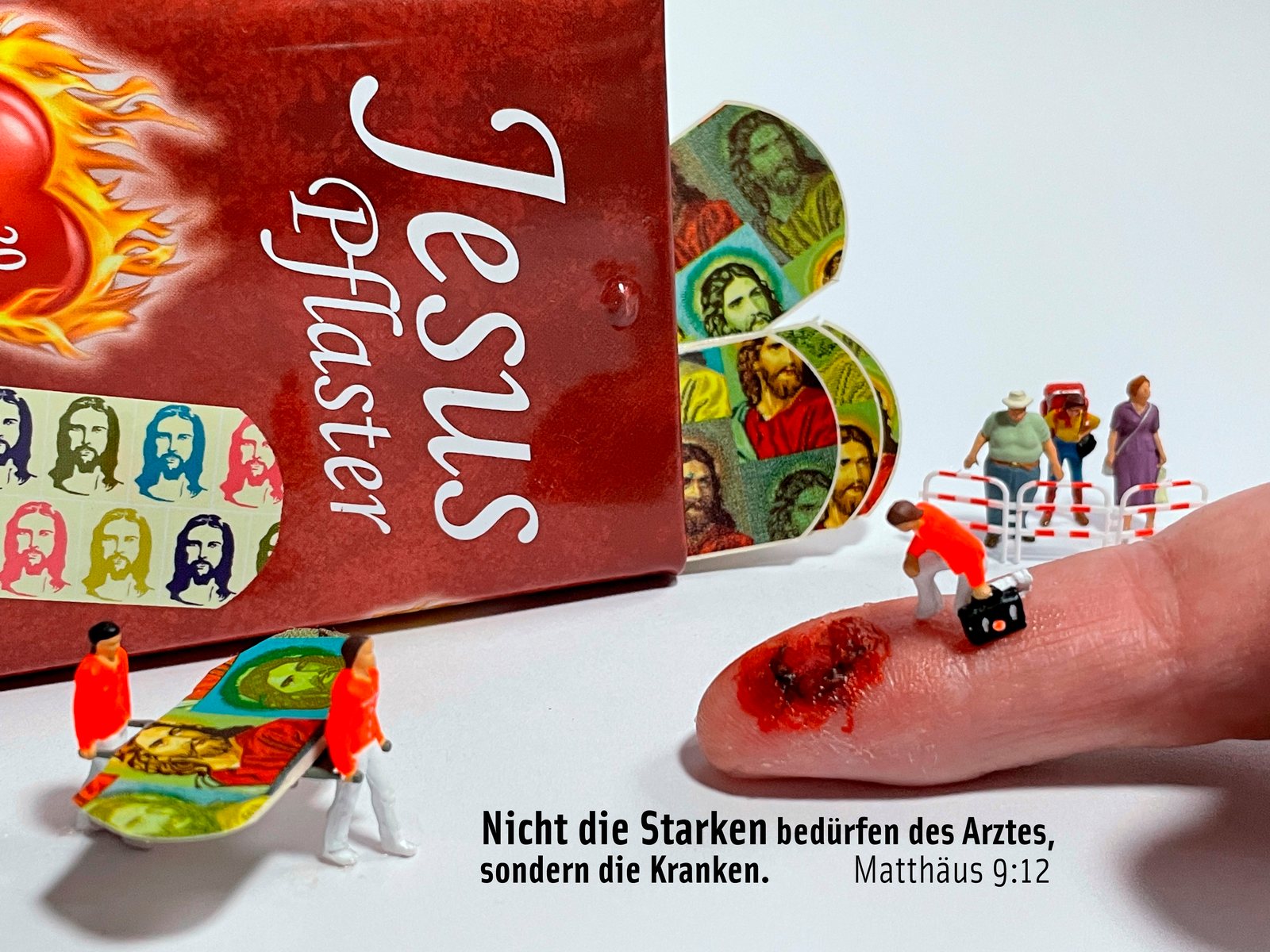 Miniatur-Sanitäter versorgen eine Schnittwunde an einem Finger, daneben eine Packung „Jesus Pflaster“, dazu Matthäus 9,12: „Nicht die Starken bedürfen des Arztes, sondern die Kranken.“