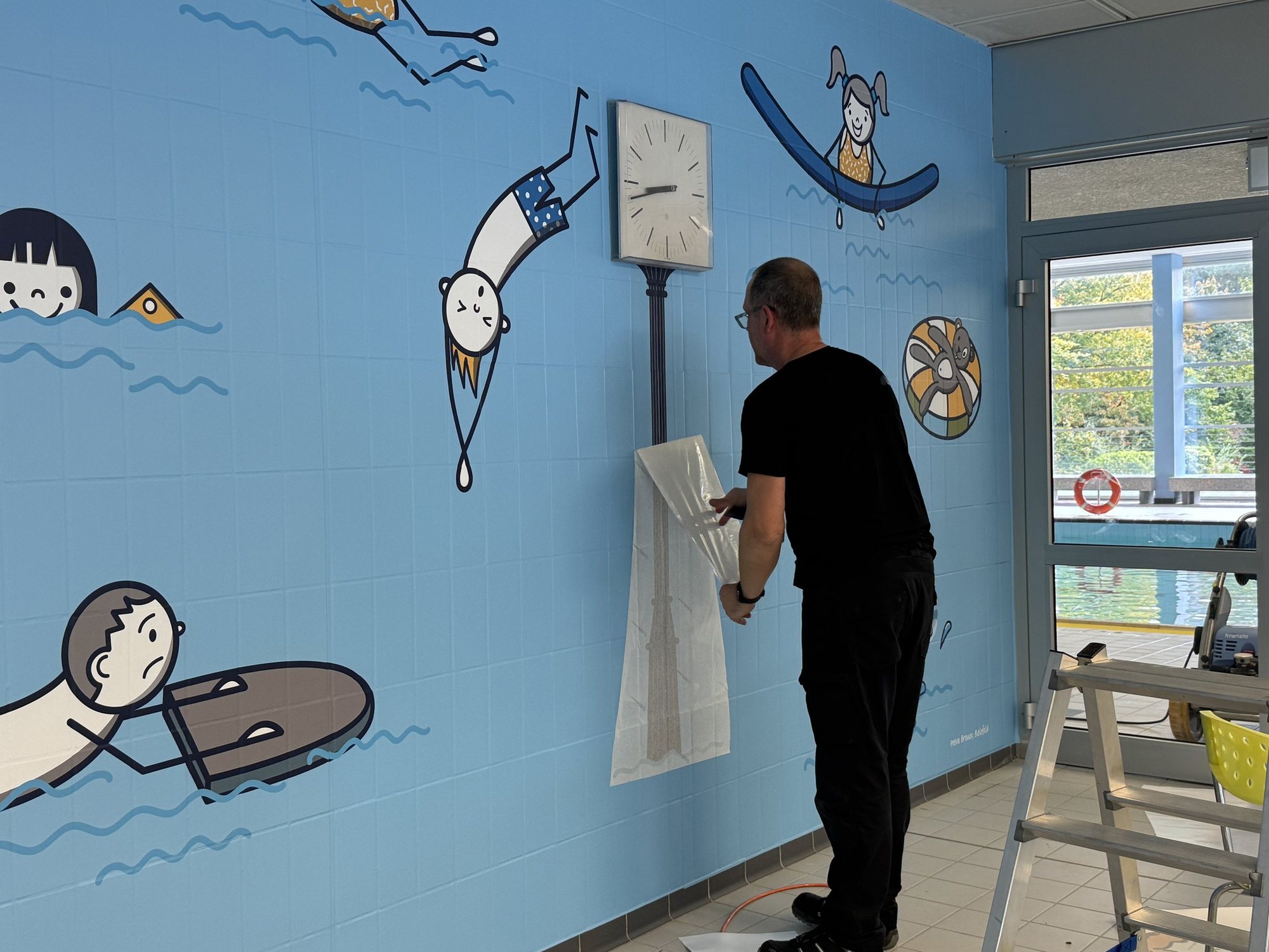 Making-of: Die Folie mit den Figuren wird an der hellblauen Wand angebracht